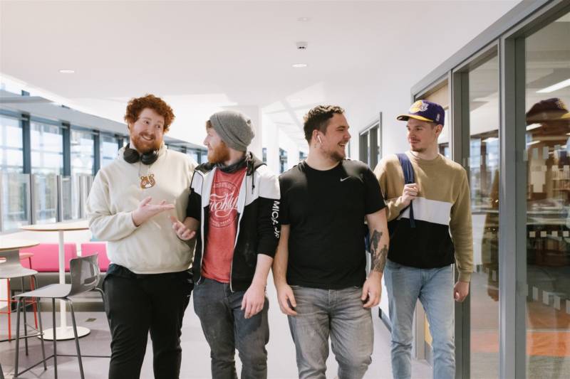Four smiling male students walking through South West College campus