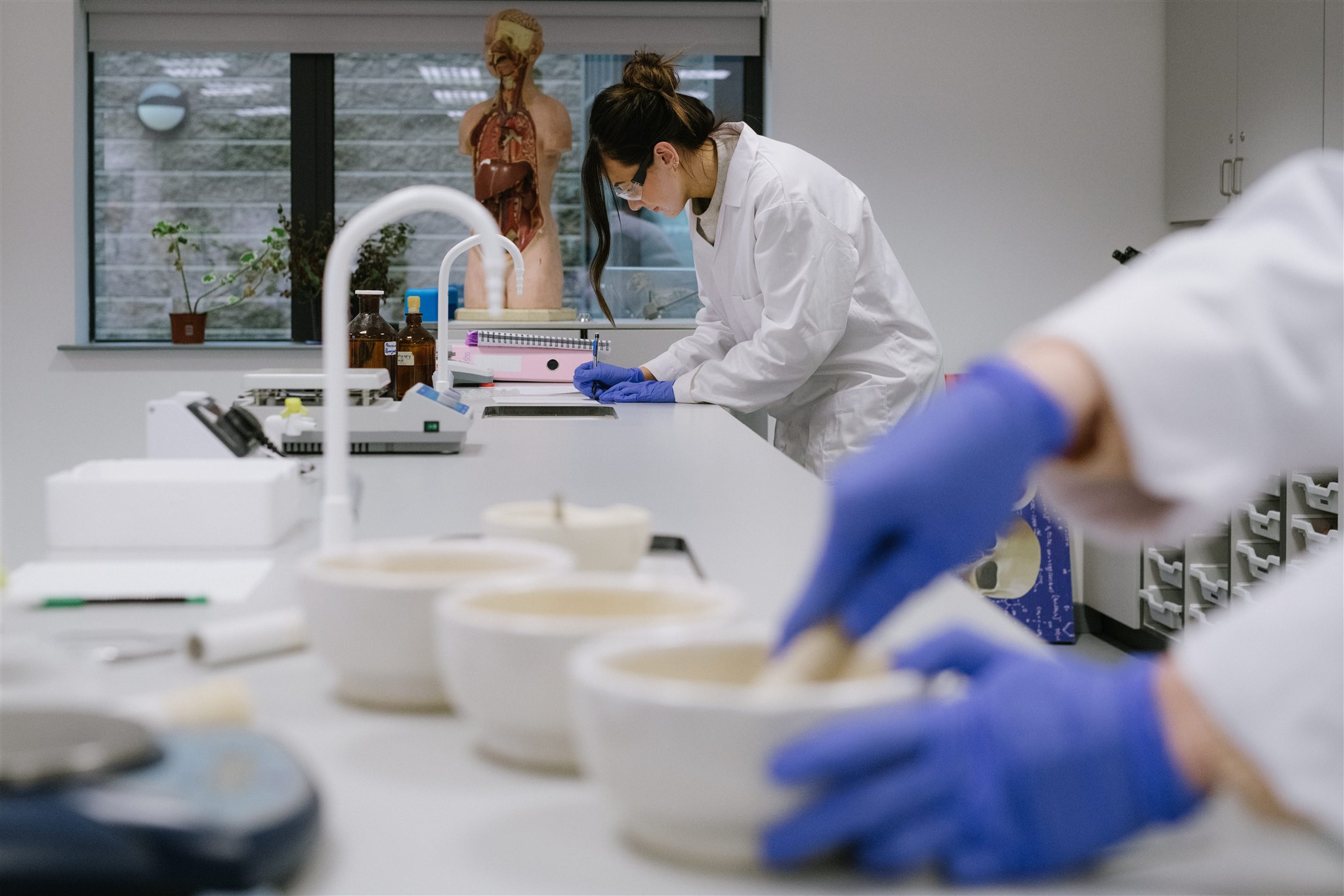 South West College science lab, students are wearing white lab coats and science equipment such as microscopes