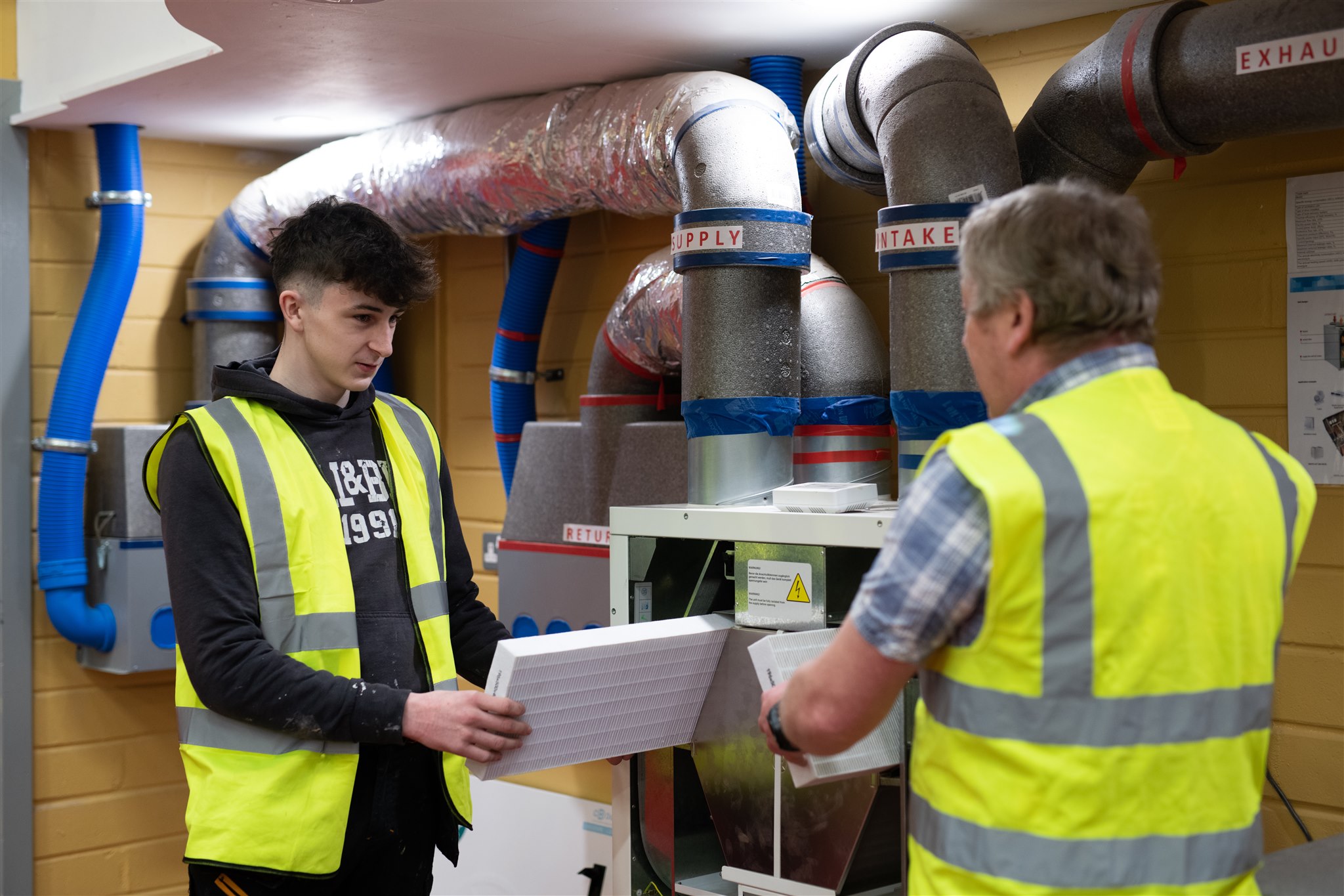 South West College construction and trades student with lecturer in workshop wearing high-vis jackets