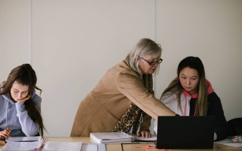 South West College students working at desk, one is one a laptop and being helped by a member of SWC staff